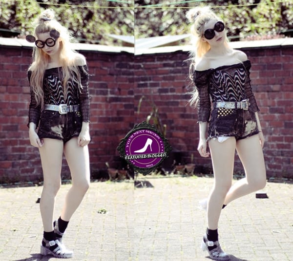 Kayla channels grunge glam with a psychedelic off-shoulder top, studded belt, edgy distressed shorts, oversized round sunglasses, and transparent jelly sandals for a bold statement look