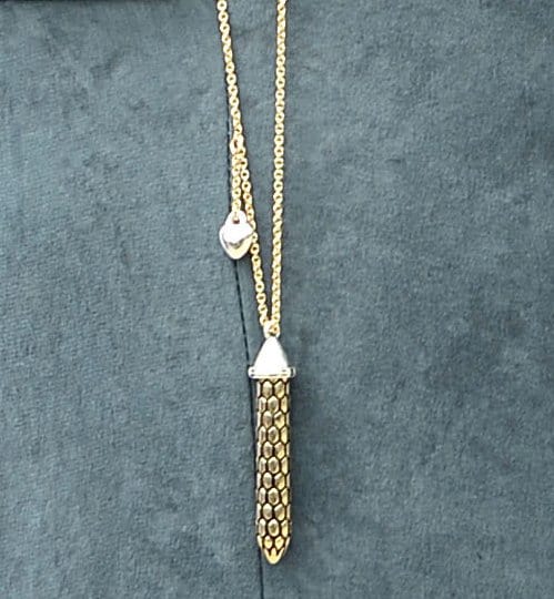 Detailed view of Nikki Reed's 7 For All Mankind x Nikki Reed Humility Necklace, featuring an antique gold column pendant with a silver heart