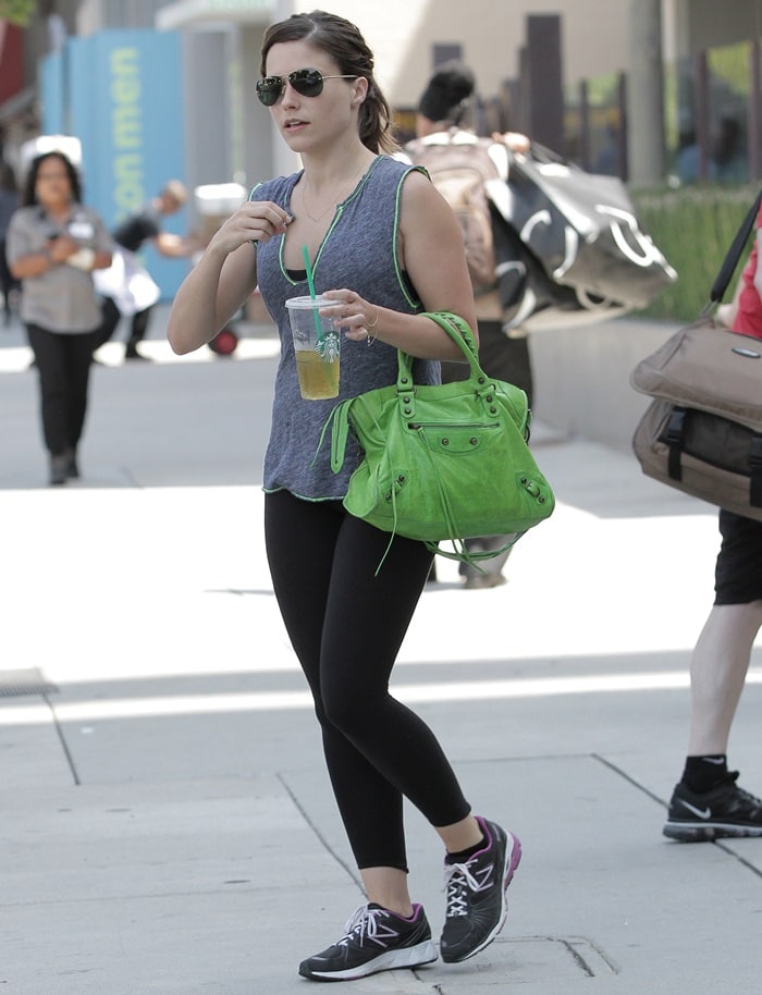 Sophia Bush looks casually chic in a sporty outfit, complete with a vibrant green handbag and sunglasses, sipping on a cold drink