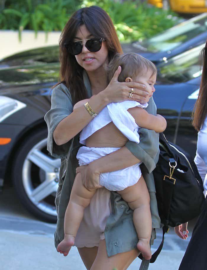 Elegantly juggling motherhood, Kourtney Kardashian pairs a military jacket with a trendy Prada baby bag on a playdate