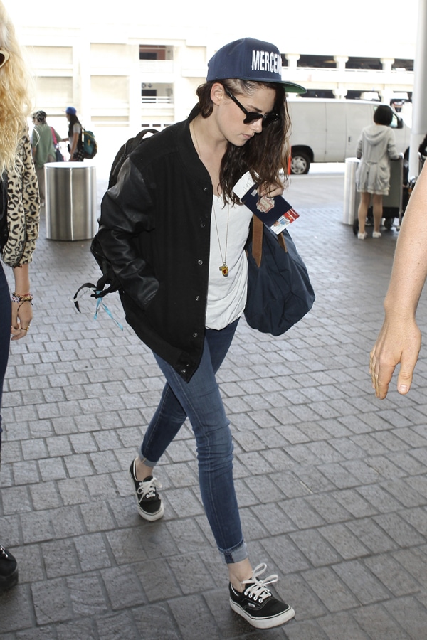 Captured on arrival at LAX, Kristen Stewart sports a relaxed ensemble perfect for travel, including a loose shirt, denim jeans, and her signature 'Mercenaries' hat, reflecting her unique style on August 19, 2013