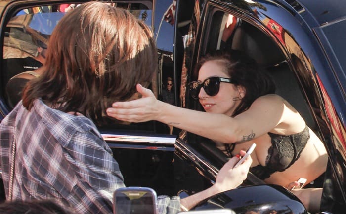 Lady Gaga leans out of her car window to warmly greet a fan in West Hollywood, wearing a bold black lace bra, oversized sunglasses, and signature edgy confidence