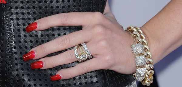 A close-up of Miley Cyrus’s hand, highlighting her breathtaking 3.5-carat diamond engagement ring from Liam Hemsworth, paired with bold red nails and a chunky gold bracelet for added edge