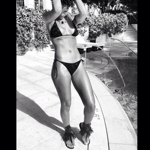 Rihanna effortlessly combines beachwear with high-fashion edge, showcasing a sleek black bikini paired with bold, fringe-detailed Ancient Greek Sandals for a striking poolside look
