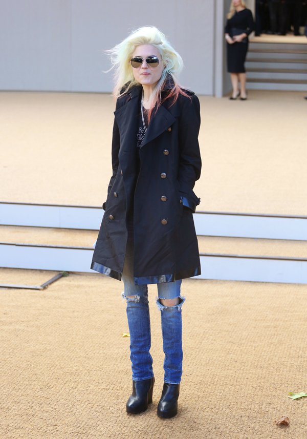 Alison Mosshart brings rocker edge to the Burberry show in a navy trench coat, distressed skinny jeans, and sleek black platform boots—blending grunge attitude with upscale tailoring