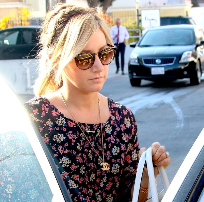 Ashley Tisdale adds a touch of effortless charm to her casual look with a floral dress, layered gold necklaces, and oversized tortoiseshell sunglasses
