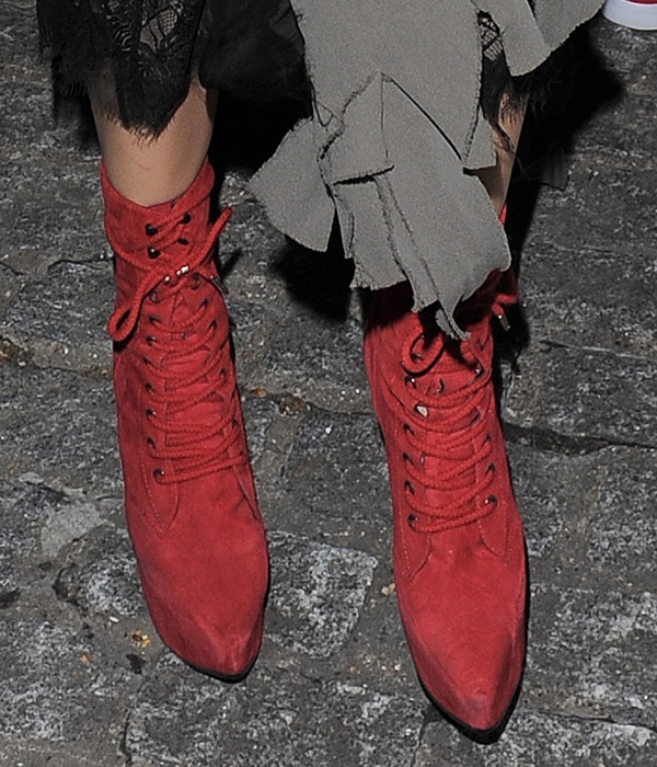 Georgia May Jagger wears red suede lace-up ankle boots with elongated pointed toes, adding a dramatic pop of color beneath her layered look