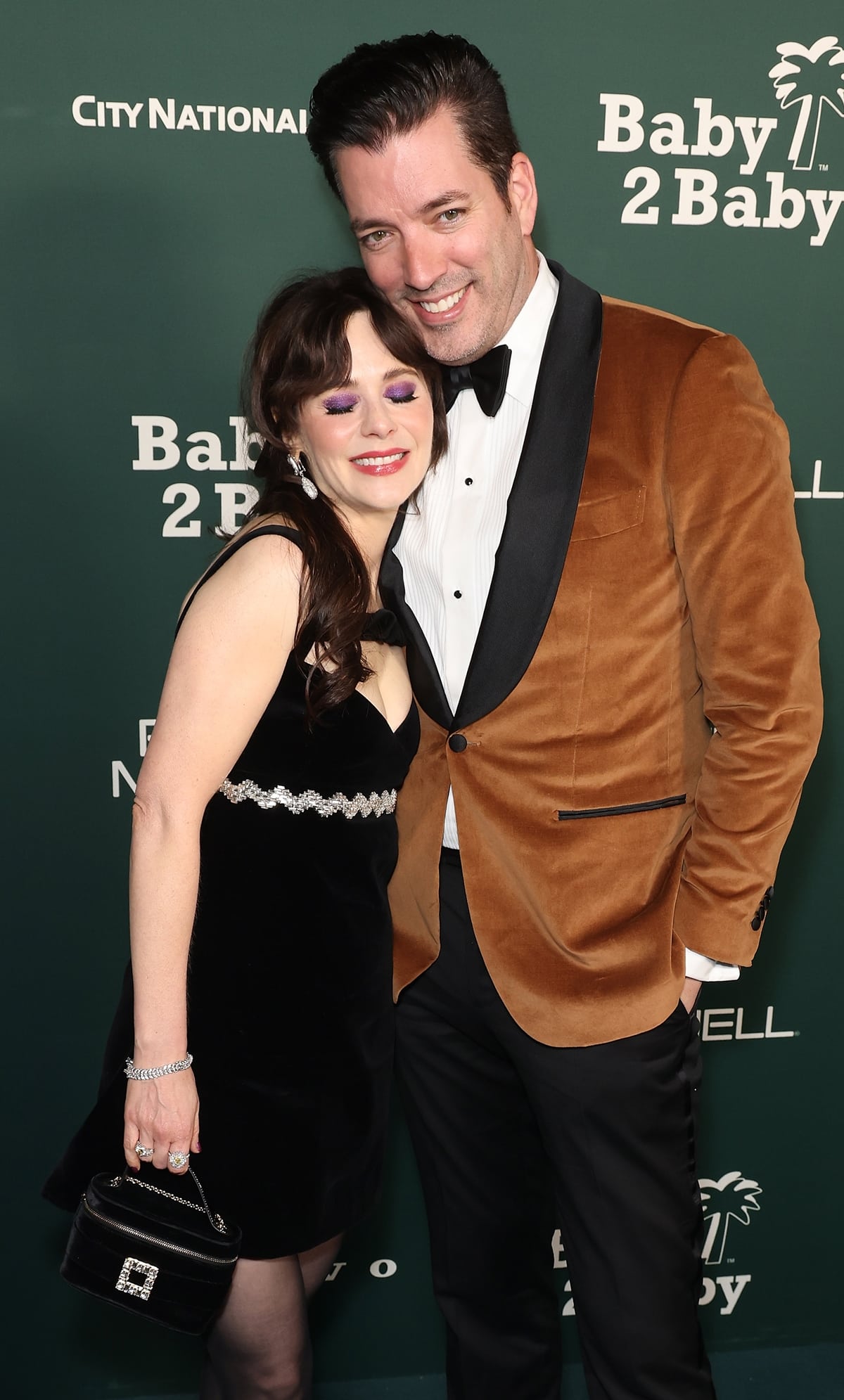 Zooey Deschanel stuns in a black velvet mini dress with a sparkling waist detail, sheer tights, and jeweled heels at the Baby2Baby Gala
