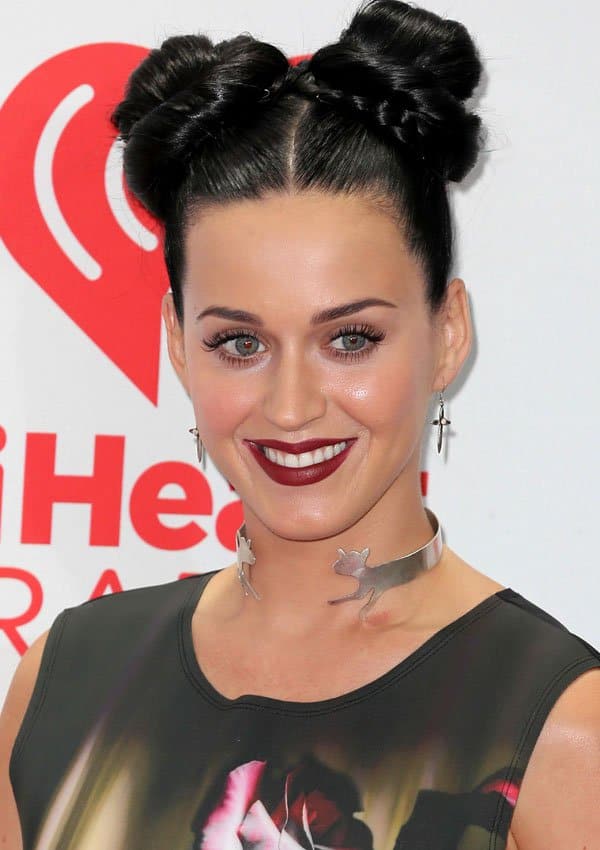 Katy Perry smiles for the cameras, highlighting her bold makeup, double-bun hairstyle, and unique animal silhouette neck cuff at the iHeartRadio Music Festival
