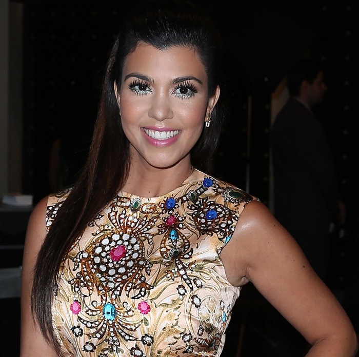 Kourtney Kardashian shines in a gold ASOS mini dress adorned with vibrant gem details, capturing the essence of glamour