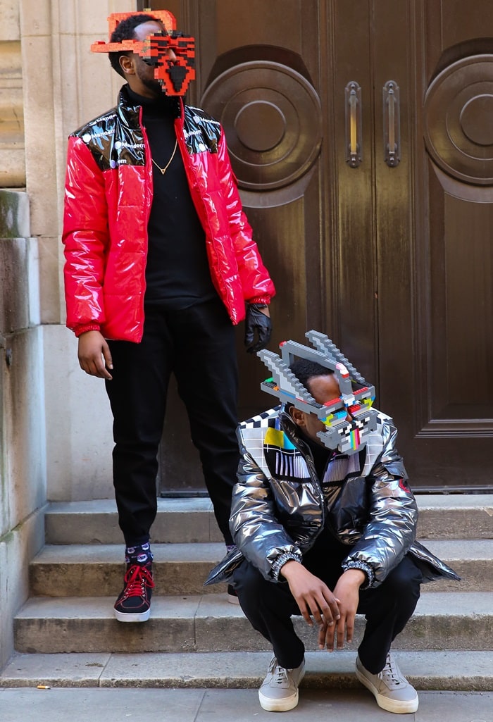 Two London Fashion Week attendees transformed LEGO bricks into futuristic face masks, pairing the playful geometric headpieces with glossy puffer jackets, slim black tailoring, and minimalist sneakers for an eye-catching street-style moment in February 2018