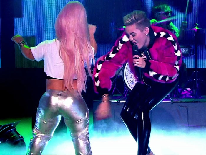 Miley Cyrus dances onstage in London during her Bangerz promo run, her glossy black leggings and towering heels enhancing the high-energy, club-inspired aesthetic