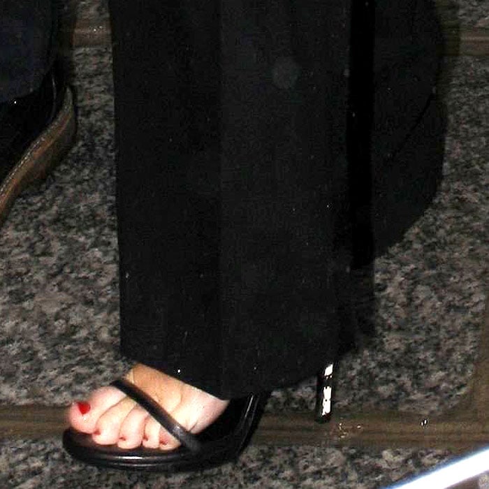 A close-up of Miley Cyrus’ feet reveals glossy red pedicure paired with sleek black ankle-strap sandals set on striking white snake-effect heels