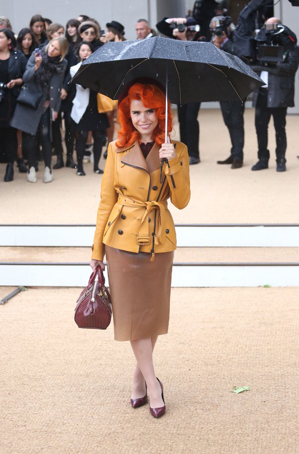 Paloma Faith embraces vintage glamour in a mustard belted trench coat and glossy burgundy pumps, pairing the look with a caramel leather pencil skirt and umbrella flair worthy of a cinematic moment