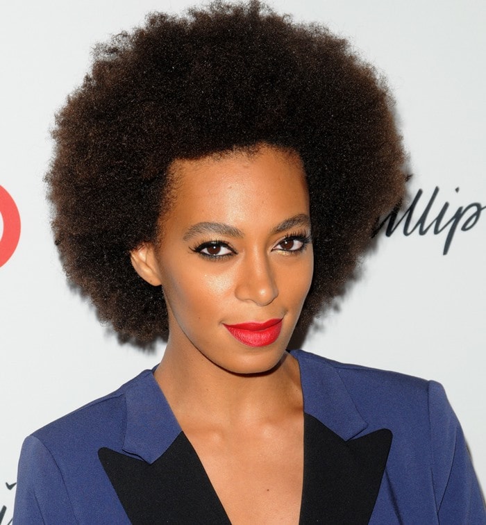 Solange Knowles completes her bold look with a voluminous natural afro, striking red lips, and dramatic winged eyeliner that highlights her eyes