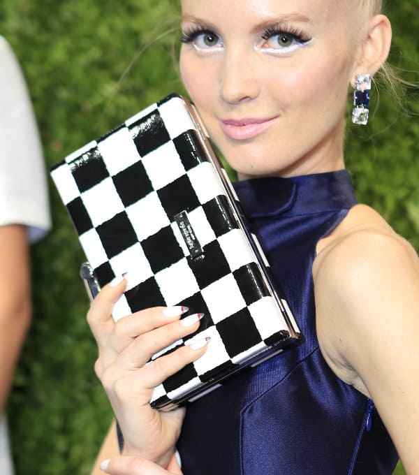 A model showcasing a black and white checkered clutch from Kate Spade, paired with a sleek navy dress and bold earrings, exuding modern elegance