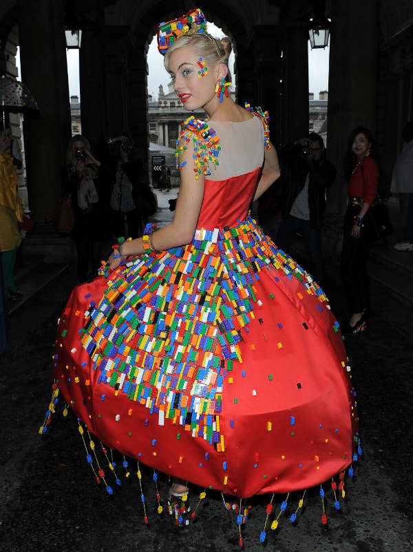 Anne-Sophie Cochevelou transformed thousands of colorful LEGO bricks into wearable couture, pairing the sculptural red satin dress with transparent wedge sandals filled with loose LEGO pieces for one of London Fashion Week’s most playful runway shoe moments