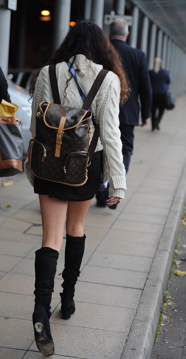 Eliza Doolittle showcased effortless fall style at Manchester Piccadilly Station on October 11, 2013, pairing a chunky knit sweater and miniskirt with knee-high suede boots and a classic Louis Vuitton backpack