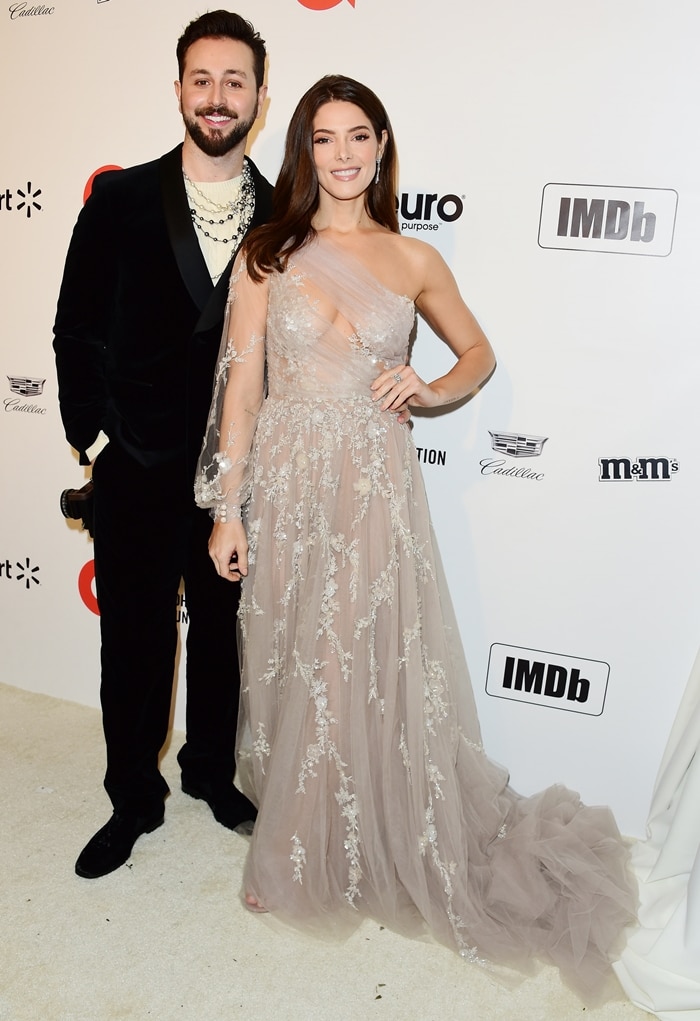 Paul Khoury and Ashley Greene exude elegance at the 28th Annual Elton John AIDS Foundation Academy Awards Viewing Party, with Paul in a sleek black velvet suit and layered chains and Ashley dazzling in a sheer, embellished one-shoulder gown on February 9, 2020, in West Hollywood, California