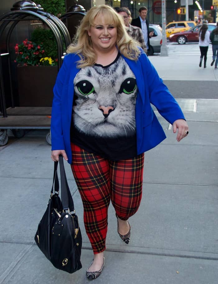 Rebel Wilson steps through New York City on September 30, 2013, anchoring her playful cat-print tee, cobalt blue blazer, and red tartan leggings with stud-embellished black flats