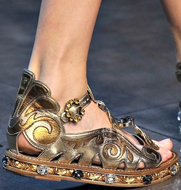 Gold Dolce Gabbana flat sandals featuring intricate cut-out designs, jeweled embellishments, and ornate detailing around the sole embodying the brand's luxurious aesthetic