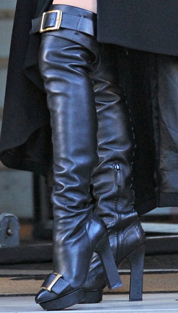 Lady Gaga's striking over-the-knee boots feature a sleek leather design, bold gold buckle detailing, side zippers for a snug fit, and a high block heel with a slight platform for added edge and sophistication