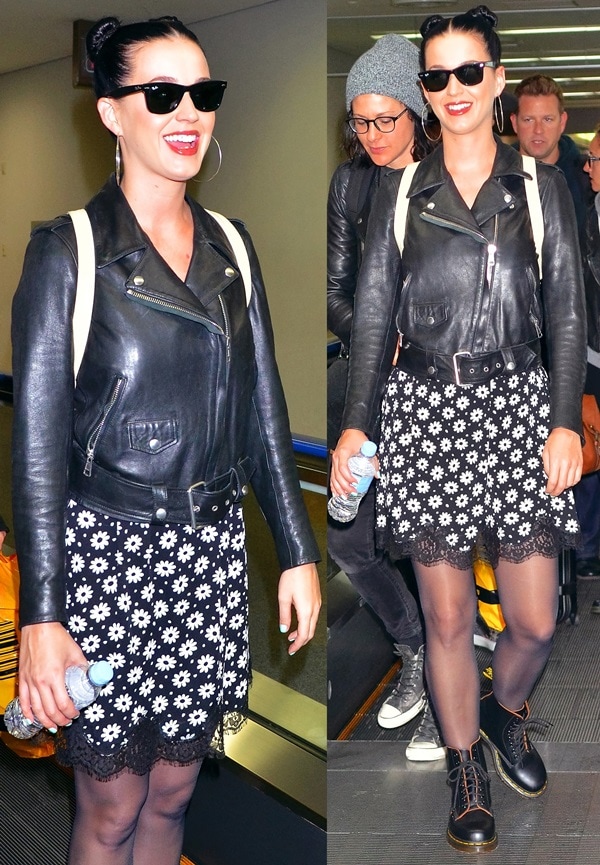 Katy Perry pairs her iconic Ray-Ban Original Wayfarer 2140 sunglasses and a black signature Acne moto jacket with a playful daisy-print dress from the Moschino Cheap Chic Resort 2014 collection and classic black Dr. Martens 1460 lace-up boots, showcasing her edgy-feminine airport style