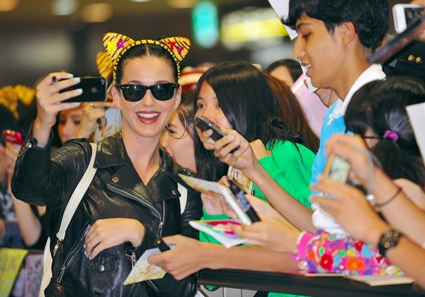 Katy Perry, sporting a playful leopard-print headband and her signature black leather moto jacket, joyfully takes selfies and interacts with fans upon her arrival in Japan