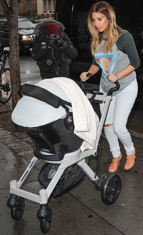 Kim Kardashian steps out in distressed white jeans and a graphic raglan tee, pairing the laid-back look with strappy Gianvito Rossi heels as she pushes baby North in her stroller