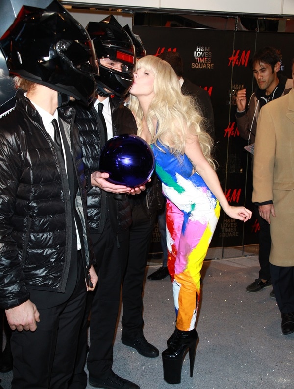 Lady Gaga added height and drama in towering black Pleaser Beyond-1020 platform ankle boots, pairing them with a hand-painted Kerin Rose Gold jumpsuit while playfully posing at the HM Times Square opening in New York City