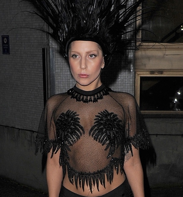 Lady Gaga stuns in a sheer black embellished crop top with fringe detailing, paired with a dramatic feathered headdress