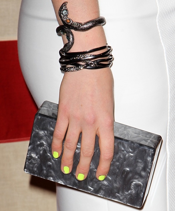 Leven Rambin adds bold accents to her look with a marbled acrylic Jean box clutch by Edie Parker, a statement snake-inspired bracelet, and a vibrant neon yellow manicure