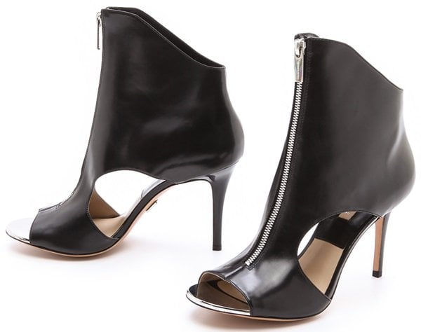 The Michael Kors Collection “Mila” booties feature sleek cutout sides, peep toes, and slim stiletto heels finished with polished silver trim and exposed back zippers