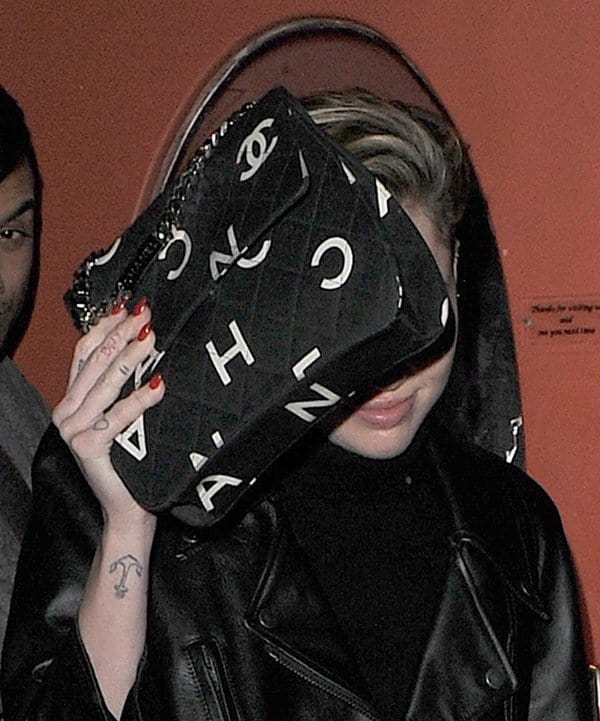 Miley Cyrus uses her vintage Chanel 1996-1997 printed jersey fold-over bag to shield her face from the paparazzi