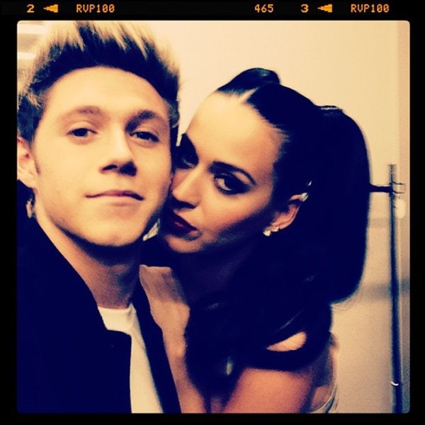 Katy Perry and Niall Horan share a playful moment, captured in a close-up that highlights Katy's dark, dramatic lip color and slicked-back hairstyle
