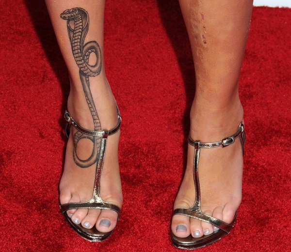 Paz de la Huerta showcases her dramatic king cobra tattoo winding up her right foot and ankle in metallic T-strap sandals, the slender straps and open-toe design framing the striking ink and her soft grey pedicure