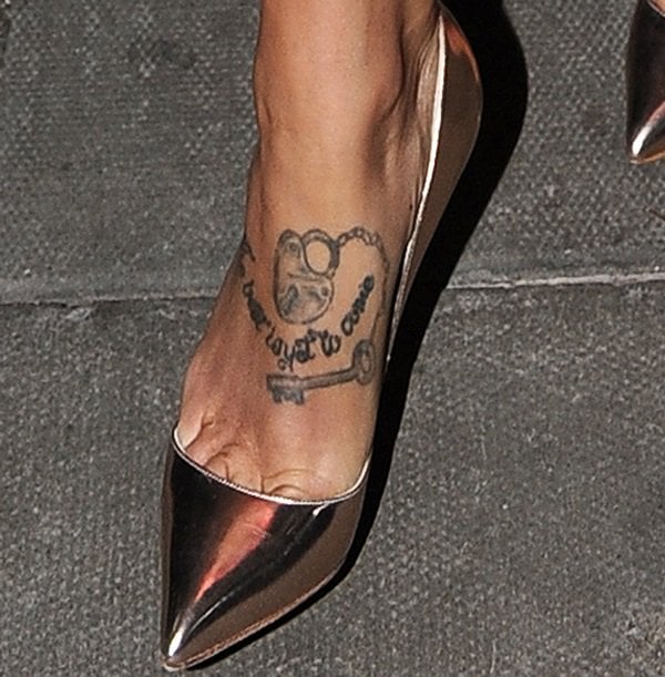 Tamara Ecclestone reveals her “The Best Is Yet to Come” foot tattoo in mirror-finish metallic pointed-toe pumps, the sleek stiletto silhouette and reflective surface drawing the eye directly to the scripted ink and softly polished toes