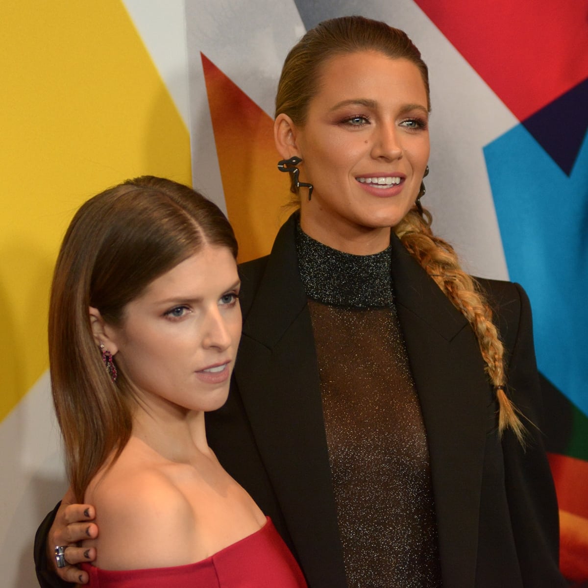 Blake Lively, towering over Anna Kendrick in a glittering sheer top and structured blazer, posed alongside her co-star, who stunned in an off-the-shoulder red gown, highlighting their striking height contrast on the red carpet