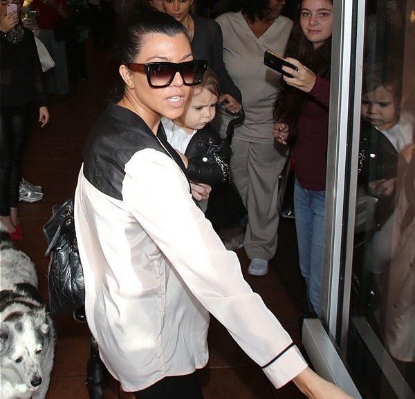 Kourtney Kardashian looked effortlessly chic in a color-block tuxedo-style blouse paired with sleek leather leggings and oversized Dita sunglasses while carrying daughter Penelope