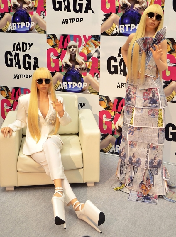 Two life-sized Gagadolls modeled after Lady Gaga showcase her iconic Artpop-era fashion — one in a spiked white pantsuit and sky-high platform heels, the other in a newspaper-print dress and matching sunglasses