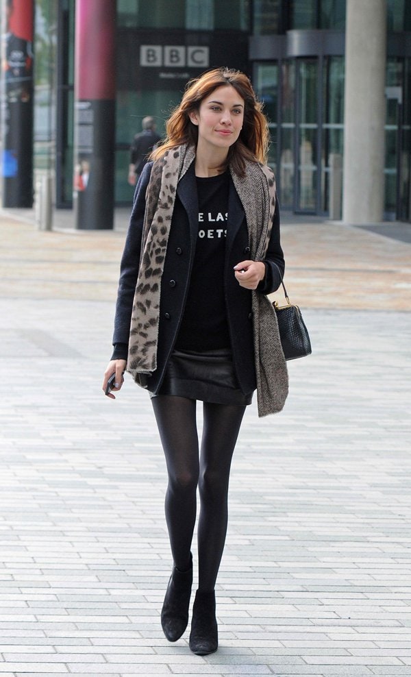 Alexa Chung layered a leopard print scarf over a black coat and leather skirt for a chic and edgy look