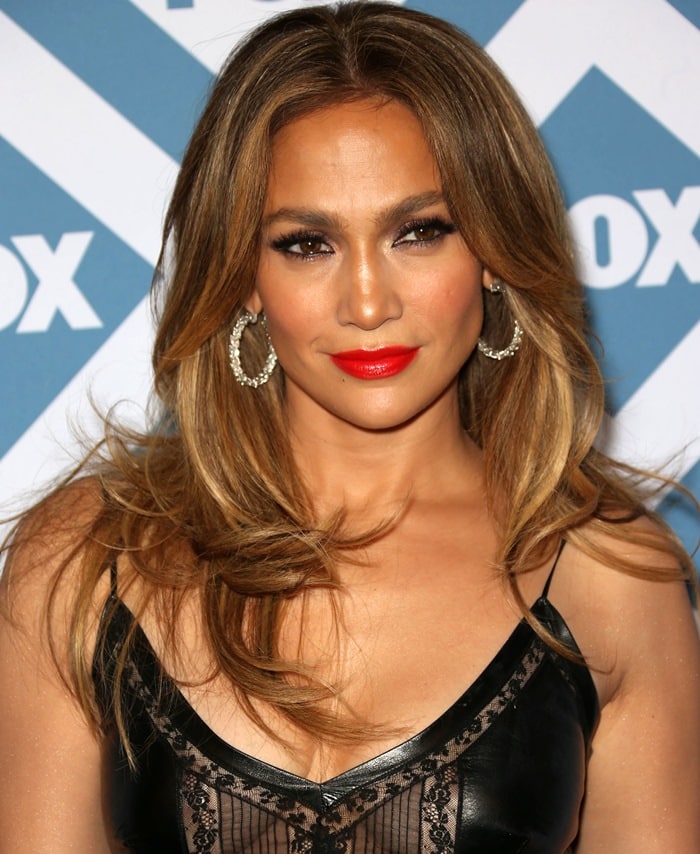 Jennifer Lopez completes her sultry look with glossy red lipstick, smoky eye makeup, and diamond hoop earrings