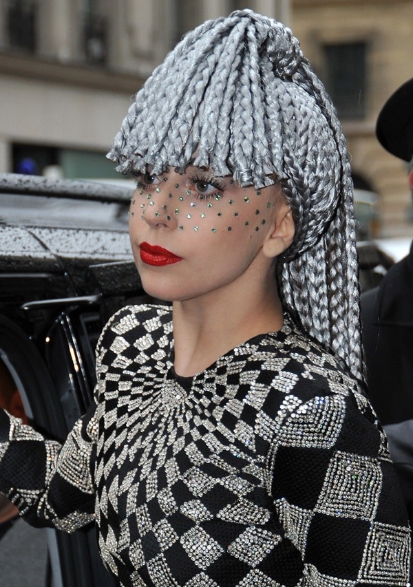Lady Gaga steps out in Paris wearing a crystal-embroidered Gianni Versace jumpsuit and metallic silver braids, accented with bold red lipstick