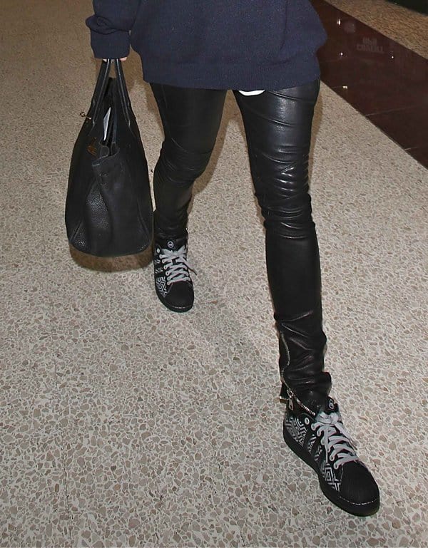 Rita Ora pairs her leather pants with a loose-fitting sweater, stylish sneakers, and a black leather tote at LAX