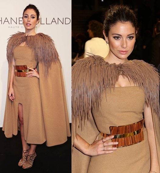 Bianca Suarez captivates in a dramatic cape dress with feathered shoulders, a statement belt, and gold strappy sandals at the Stephane Rolland show during Paris Fashion Week