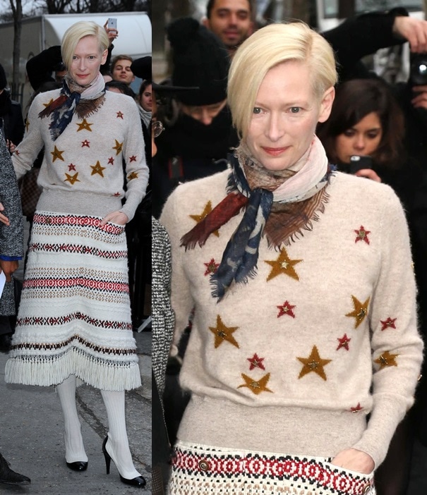 Tilda Swinton showcases her eclectic style in a star-embellished sweater, fringed skirt, and color-blocked pumps at the Chanel Haute Couture show during Paris Fashion Week