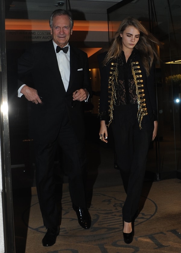 Charles Delevingne and Cara Delevingne coordinated in sleek black ensembles at Christie’s in Mayfair on February 10, 2014, with Cara elevating her look in a Balmain embroidered military knit jacket and Burberry Prorsum “Chatsworth” platform wedges