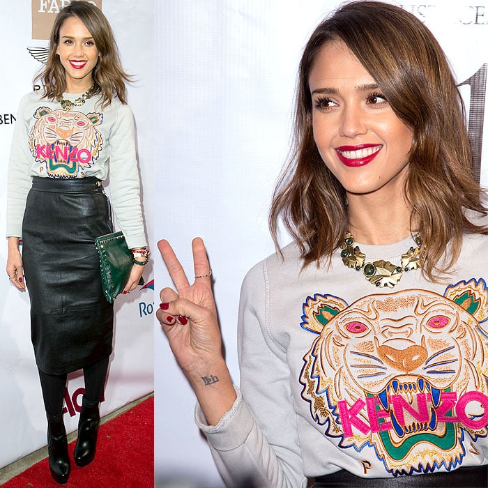 Jessica Alba styles a gray Kenzo Tiger Embroidered Cotton Sweatshirt with a sleek leather skirt, Valentino Rockstud Clutch, and Lisa Hoffman Beauty Tunisian Neroli Bracelet, blending playful streetwear and polished elegance