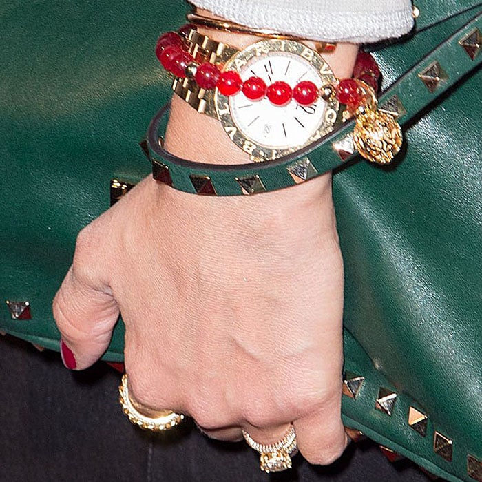 Jessica Alba adds polish with layered red beaded bracelets, a gold watch, and a stud-trimmed green clutch that echoes her outfit’s luxe-casual palette