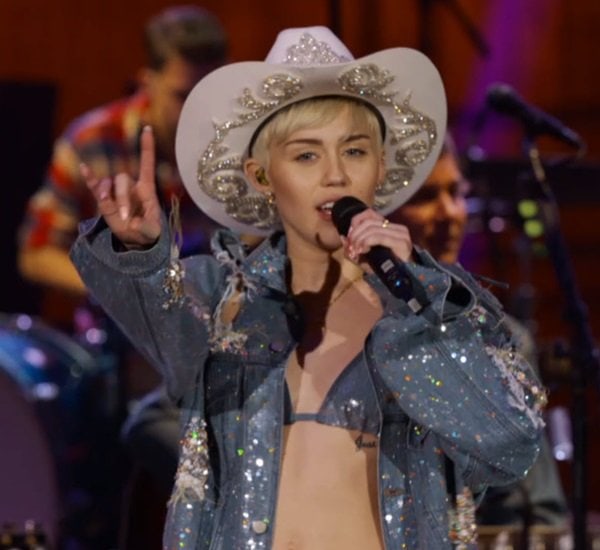 Miley Cyrus is wearing a distressed denim jacket with a bikini top